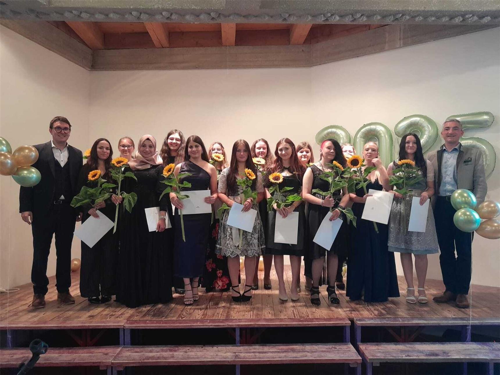 Viele Personen stehen auf einer Bühne mit Sonnenblumen in den Händen.