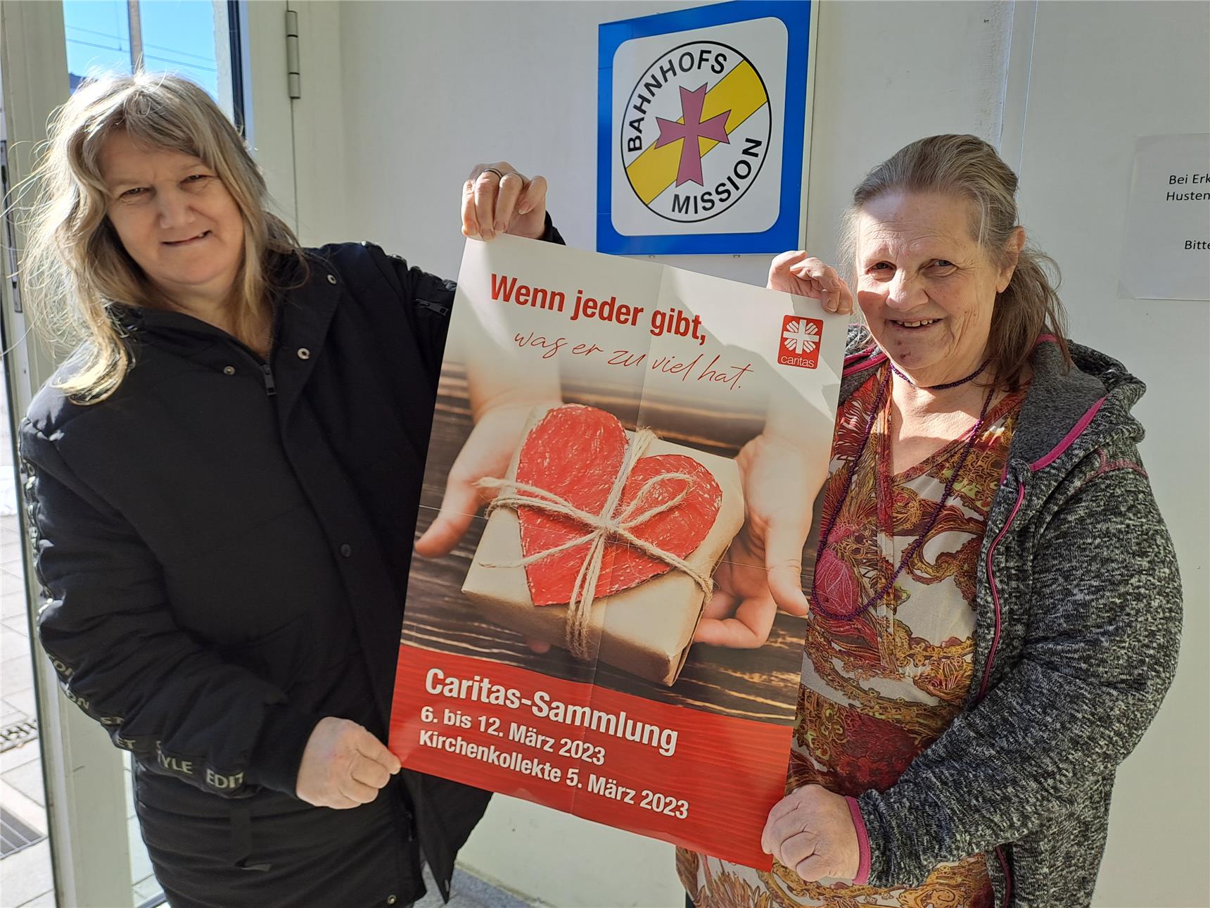 Besucher der Bahnhofsmission halten ein Plakat in die Luft