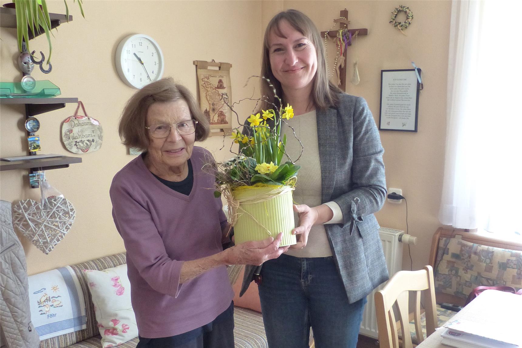 Zwei Personen stehen in einer Wohnung und halten einen Blumenstock in der Hand.