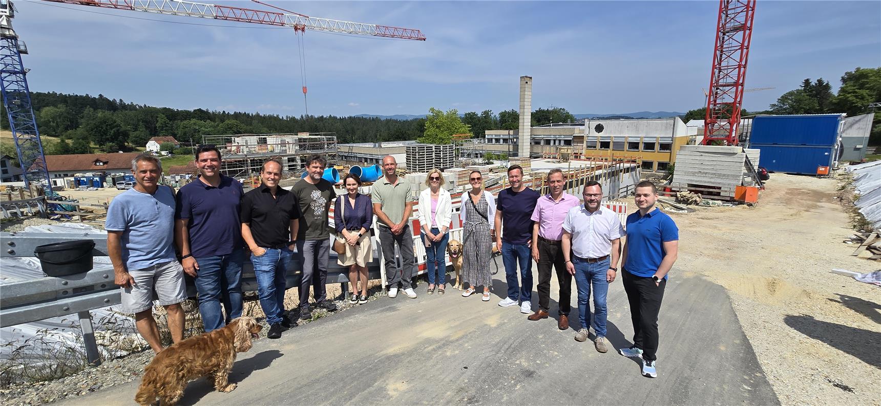 Mehrere Personen stehen auf einer erhöhten Position vor einer Baustelle und lachen in die Kamera.