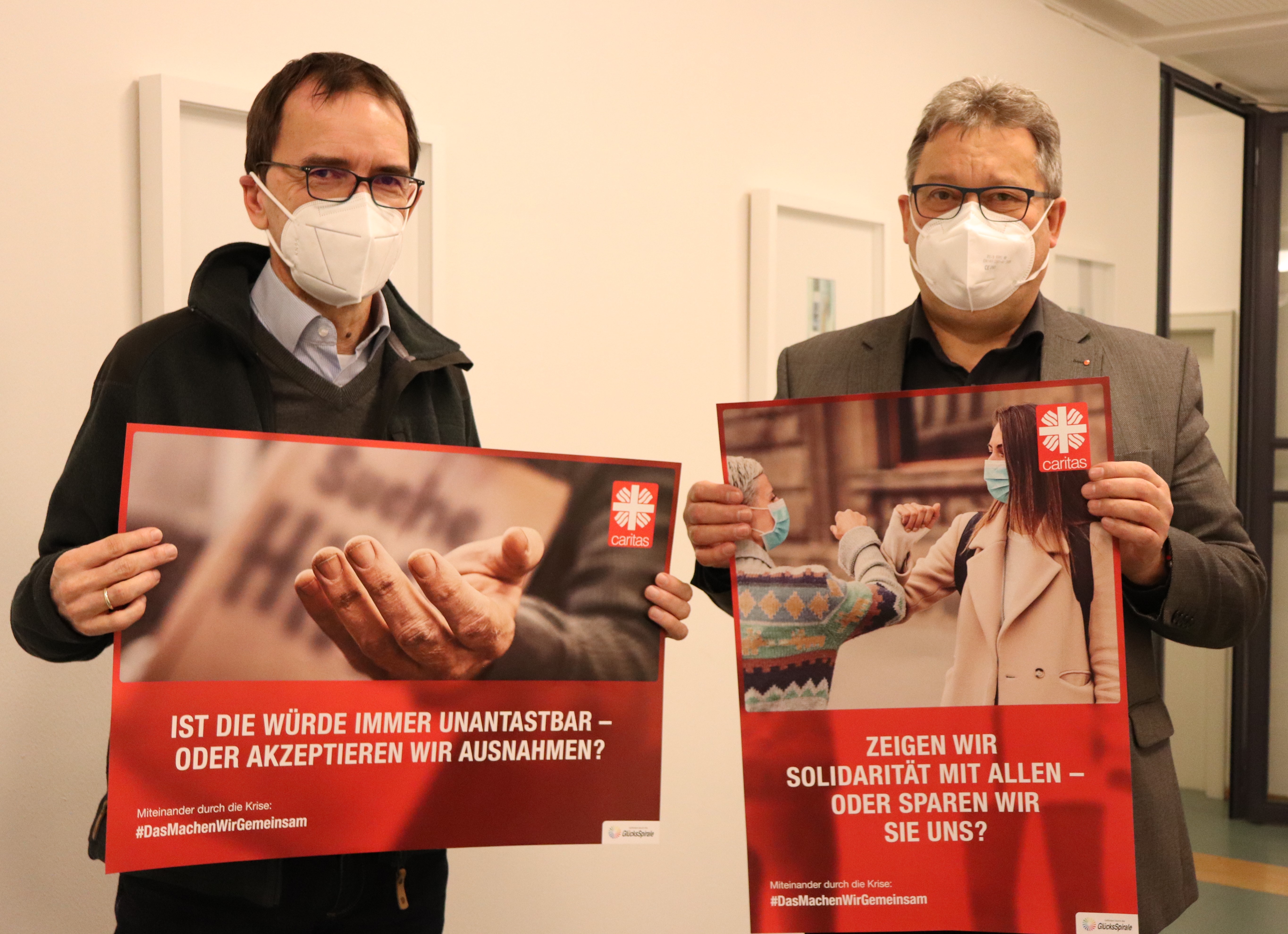 Zwei Herren halten ein Plakat zur neuen Caritas-Jahreskampagne