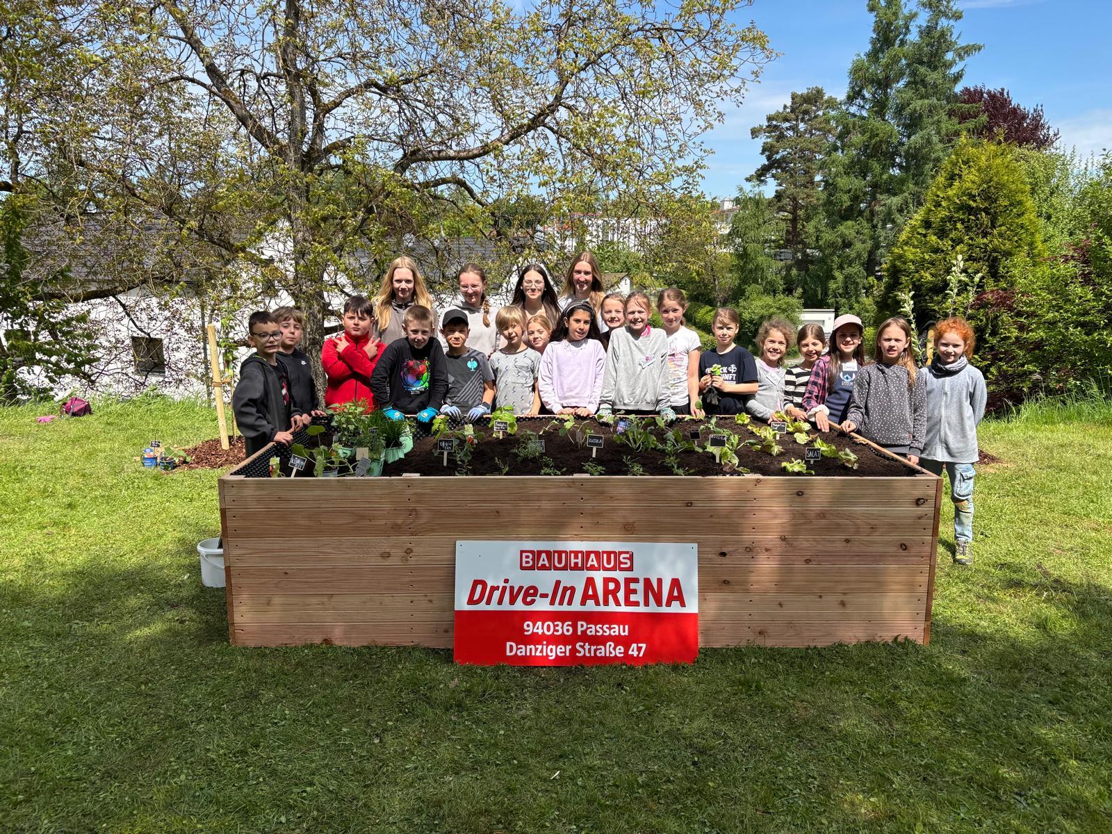 Eine Gruppenfoto von Kindern und Jugendlichen die hinter dem fertig gepflanzten Blumenbeet stehen,