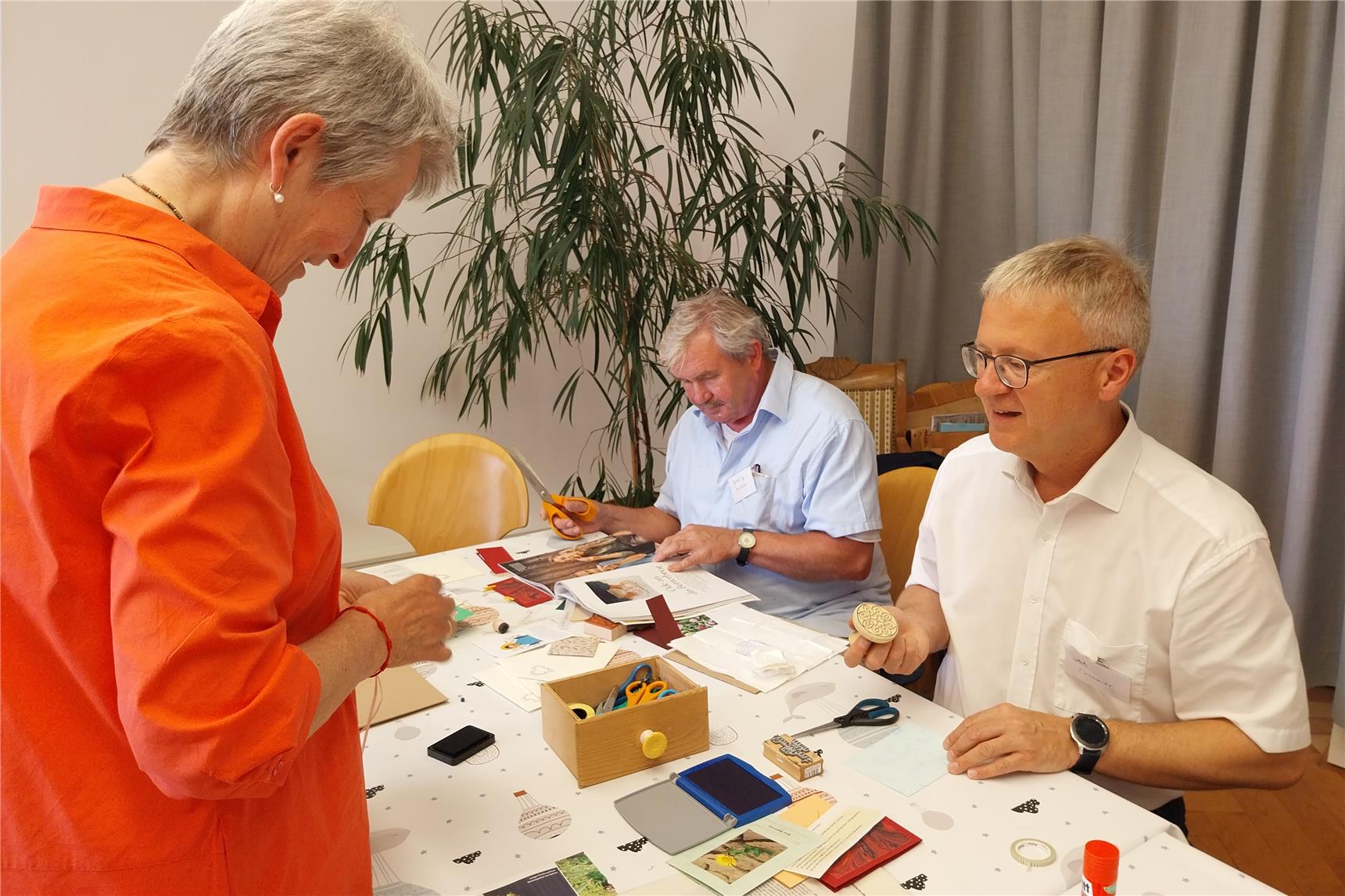 Menschen sitzen an einem Tisch, umgeben von Bastelutensilien und kreativem Material.
