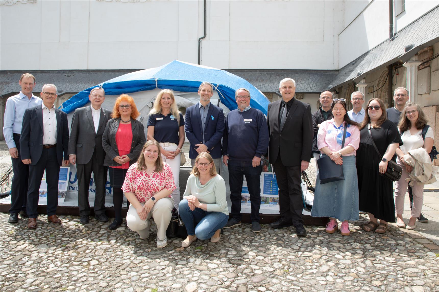 Viele Personen stehen vor einem großen Zelt in blau und weißer Farbe.