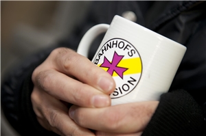 Hand hält Tasse mit Bahnhofsmissions-Logo