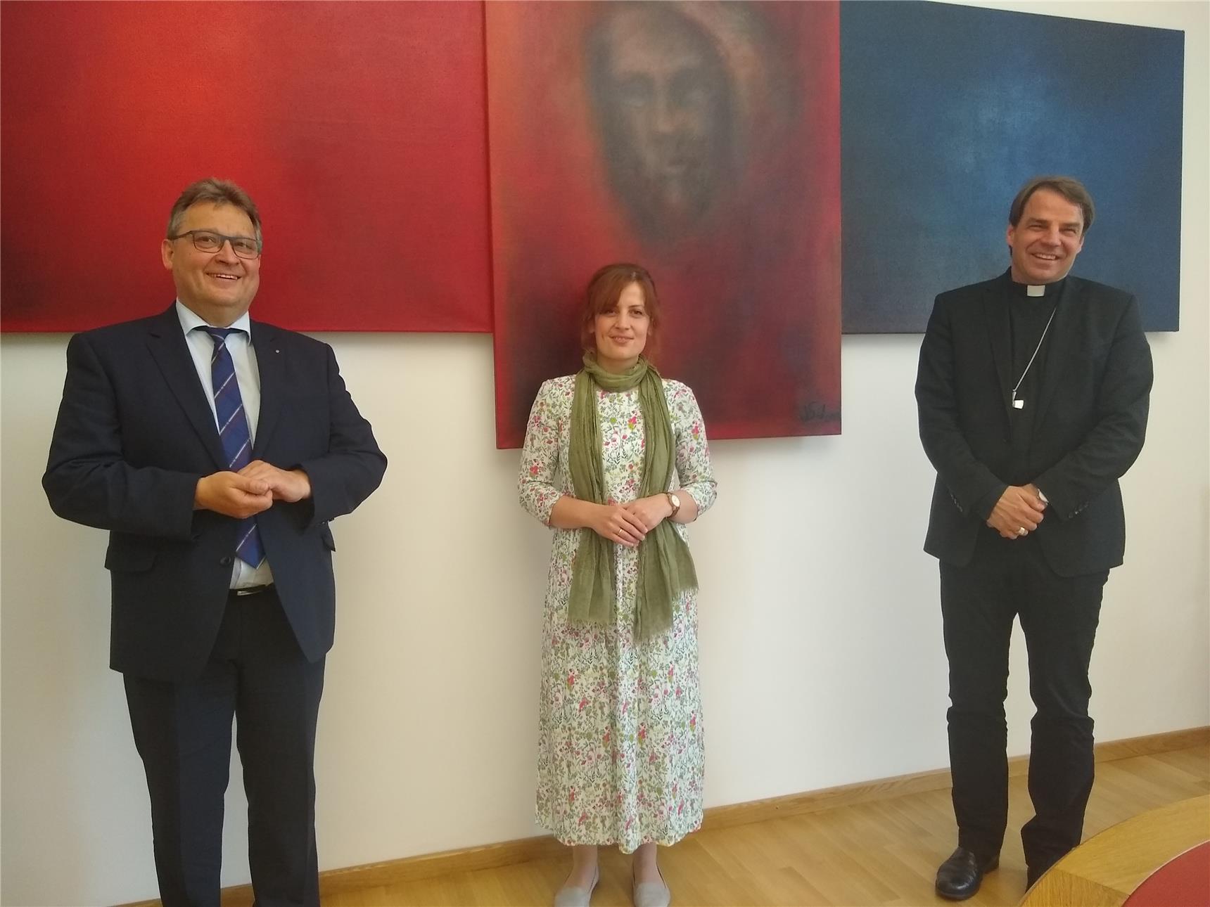 Es stehen 3 Menschen vor einer Wand, links Diakon Niederländer, in der Mitte Elke Penteker und rechts Bischof Oster