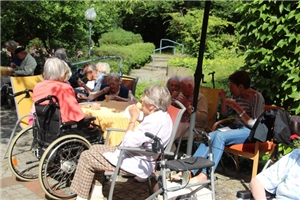 eine Gruppe von Bewohnern, zum Teil im Rollstuhl, sitzt zusammen am Tisch im Garten