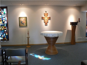 Blick in den Andachtsraum mit Kreuz, rundem Altartisch und leuchtenden Glasfenstern