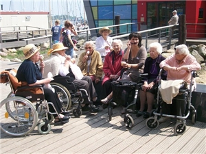 Eine Gruppe von Bewohnerinnen im Rollstuhl mit Betreuerin beim Eisschlecken am Hafen von Eckernförde.
