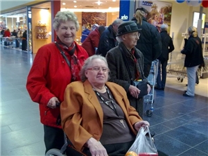 Eine ehrenamtliche Helferin begleitet eine Bewohnerin im Rollstuhl beim Einkaufen in der Innenstadt.