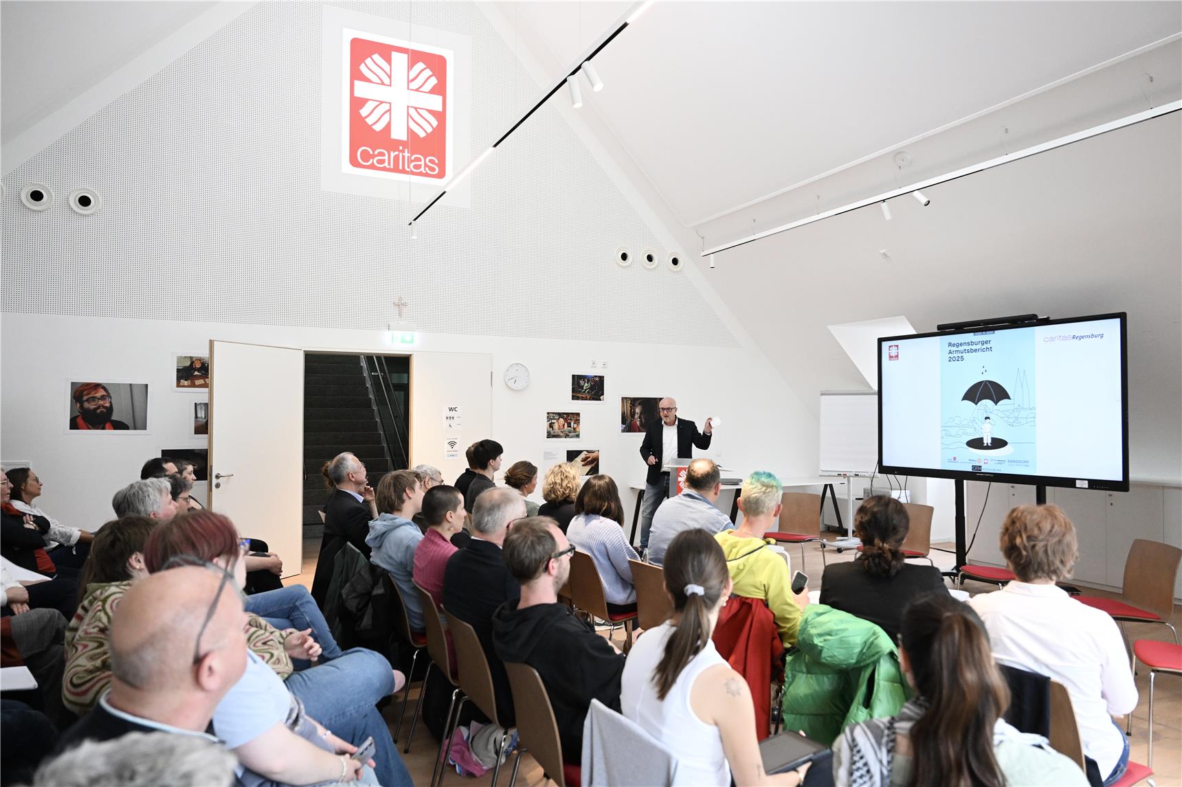 Rund 50 Menschen sitzen in einem Konferenzsaal, ein Mann moderiert vorne
