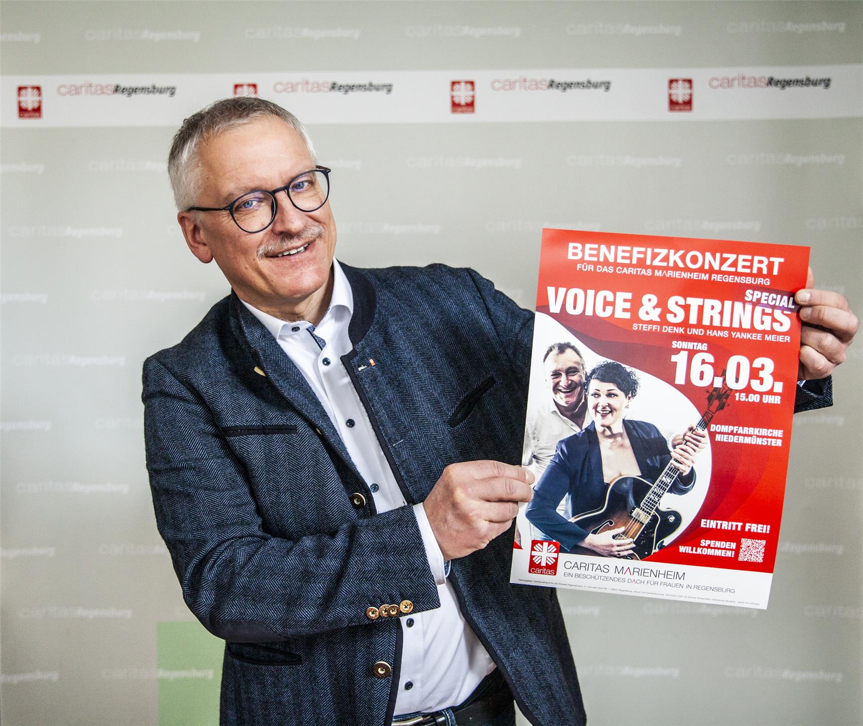 Caritasdirektor Michael Weißmann hält das Poster zum Benefizkonzert hoch