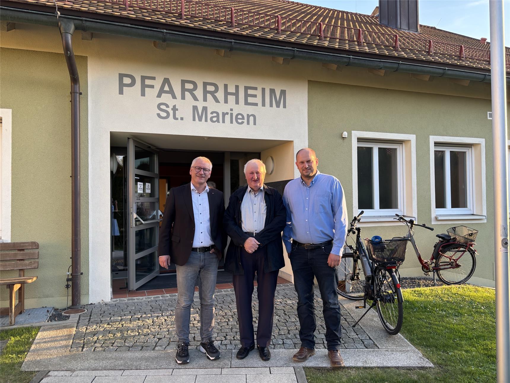 drei Männer stehen vor einem Pfarrheim