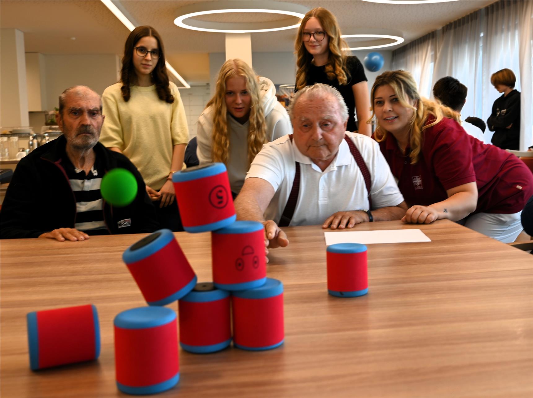 Schaumdosen im Vordergrund zur Pyramide gestapelt. Dahinter Alt und Jung die spielen.