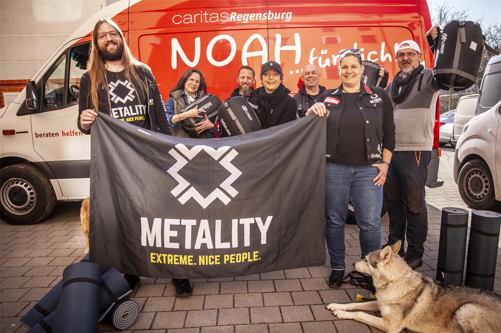Die Mitglieder von Metality e. V. stehen mit den Vertretern der Caritas vor dem Marienheim und zeigen die vielen Sachspenden mit Flagge.