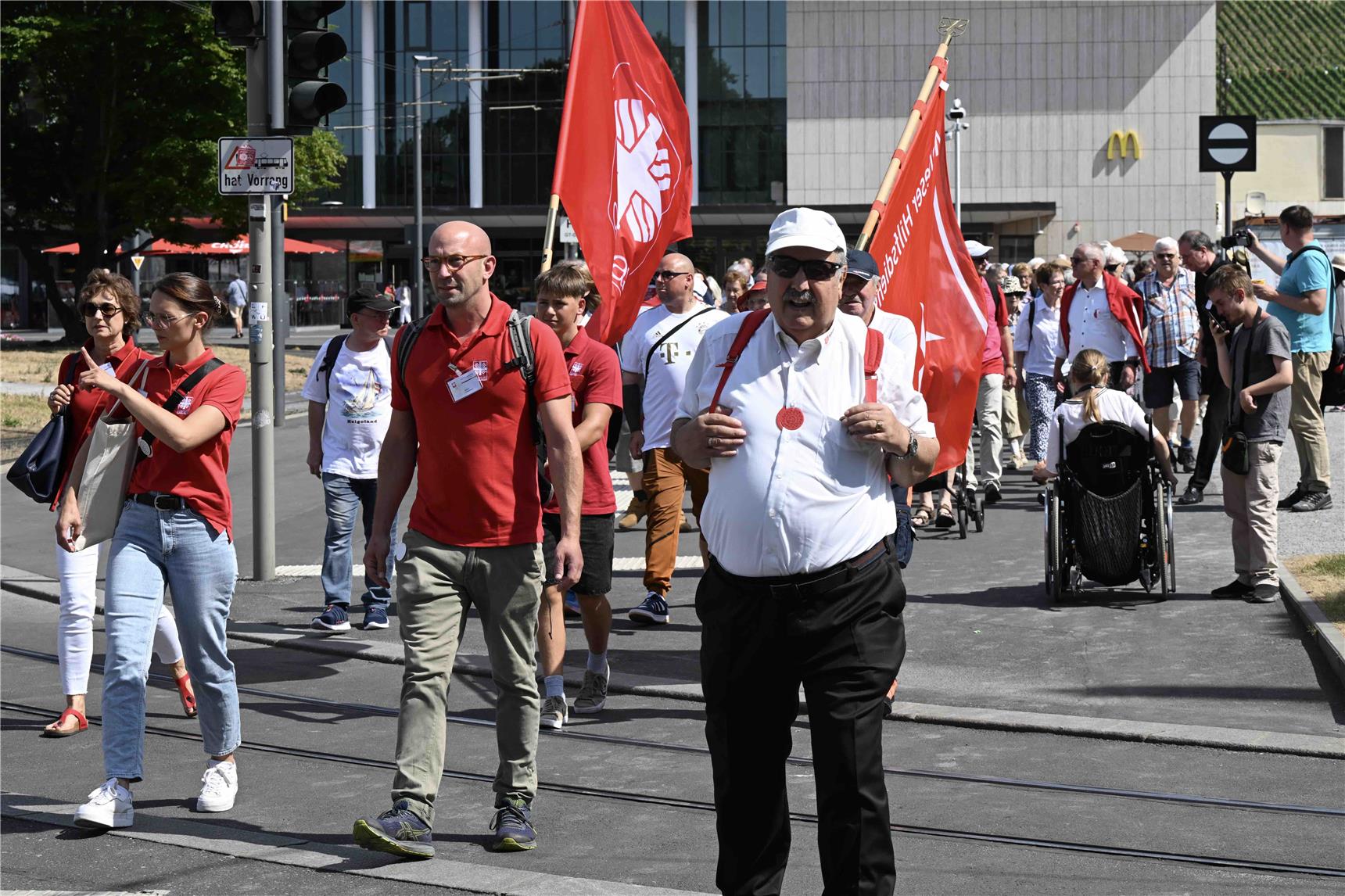 Menschen mit Caritasflagge und Caritas-T-Shirts laufen eine Straße entlang.