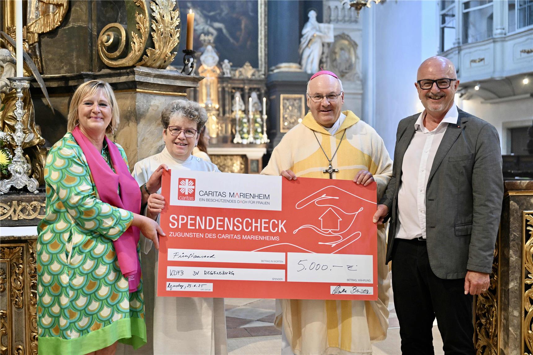 Man sieht die vier Beteiligten für die Spendenübergabe in der Kirche mit einem symbolischen Spendenscheck.