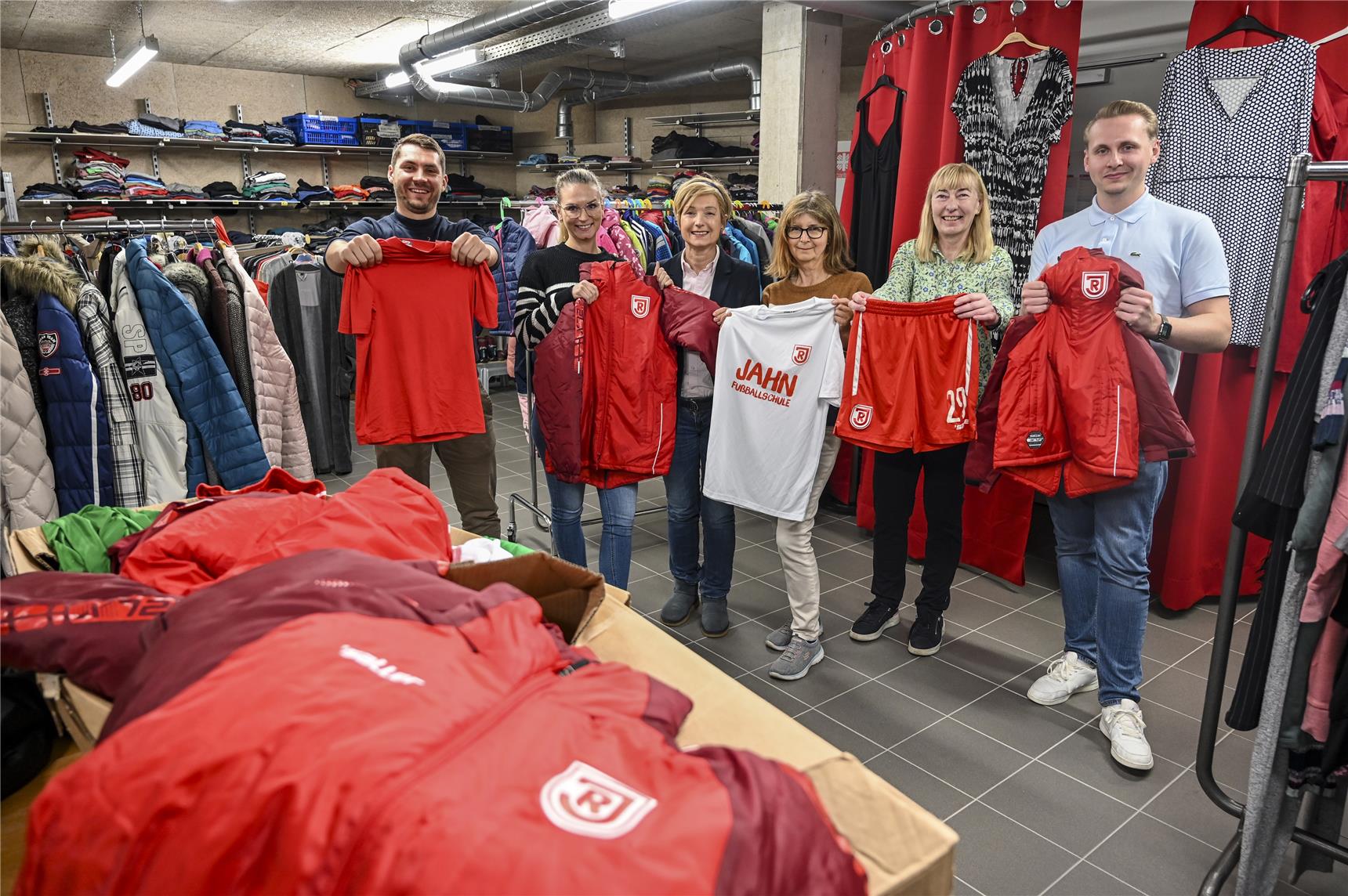 Das Team der Caritas und Vertreter vom SSV Jahn zeigen glücklich die Kleiderspende