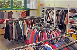 Blick in einen Raum mit einer Schrankwand und verschiedenen Kleiderständern voller Kleider.
