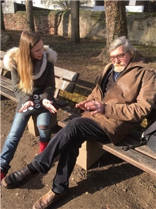 Eine junge Frau spricht auf einer Parkbank mit einem älteren Mann.