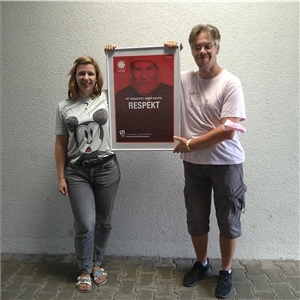 eine Frau und ein Mann stehen vor einer weißen Wand. Sie halten ein rotes Plakat mit der Aufschrift "Respekt" fest.