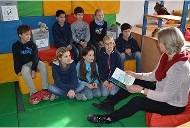 Kinder sitzen in der Gruppe auf dem Boden und bekommen etwas vorgelesen