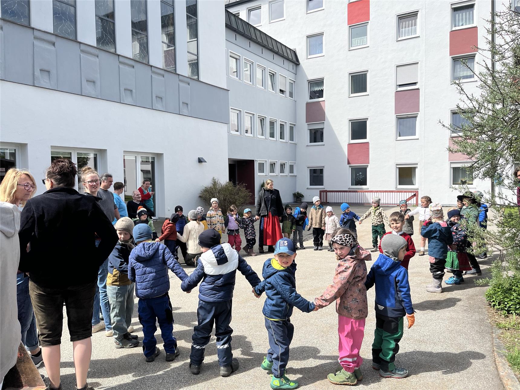 Kinder des Waldkindergartens Freyung tanzen beim Maifest im Garten des Caritas-Seniorenheims St. Gunther, während Senioren und Mitarbeitende zusehen.