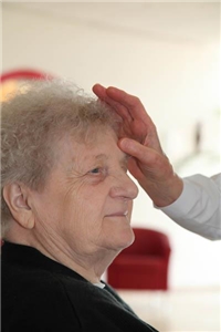 Ältere Frau erhält Kreuzzeichen auf die Stirn.