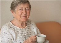 Alleinstehende Menschen, vor allem Personen, die nicht mehr so mobil sind, sind auf Unterstützung angewiesen. Ältere Dame mit einer Tasse in der Hand schaut in die Kamera. Sie hat einen skeptischen, sorgenvollen Blick