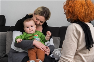 Frau Mahmuti mit ihrem kleinen Sohn und Caritasmitarbeiterin Christiane Thömmes sitzen auf einem Sofa.