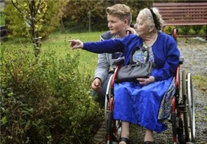 Ältere Dame im Rollstuhl wird mit Jugendlichem im Grünen
