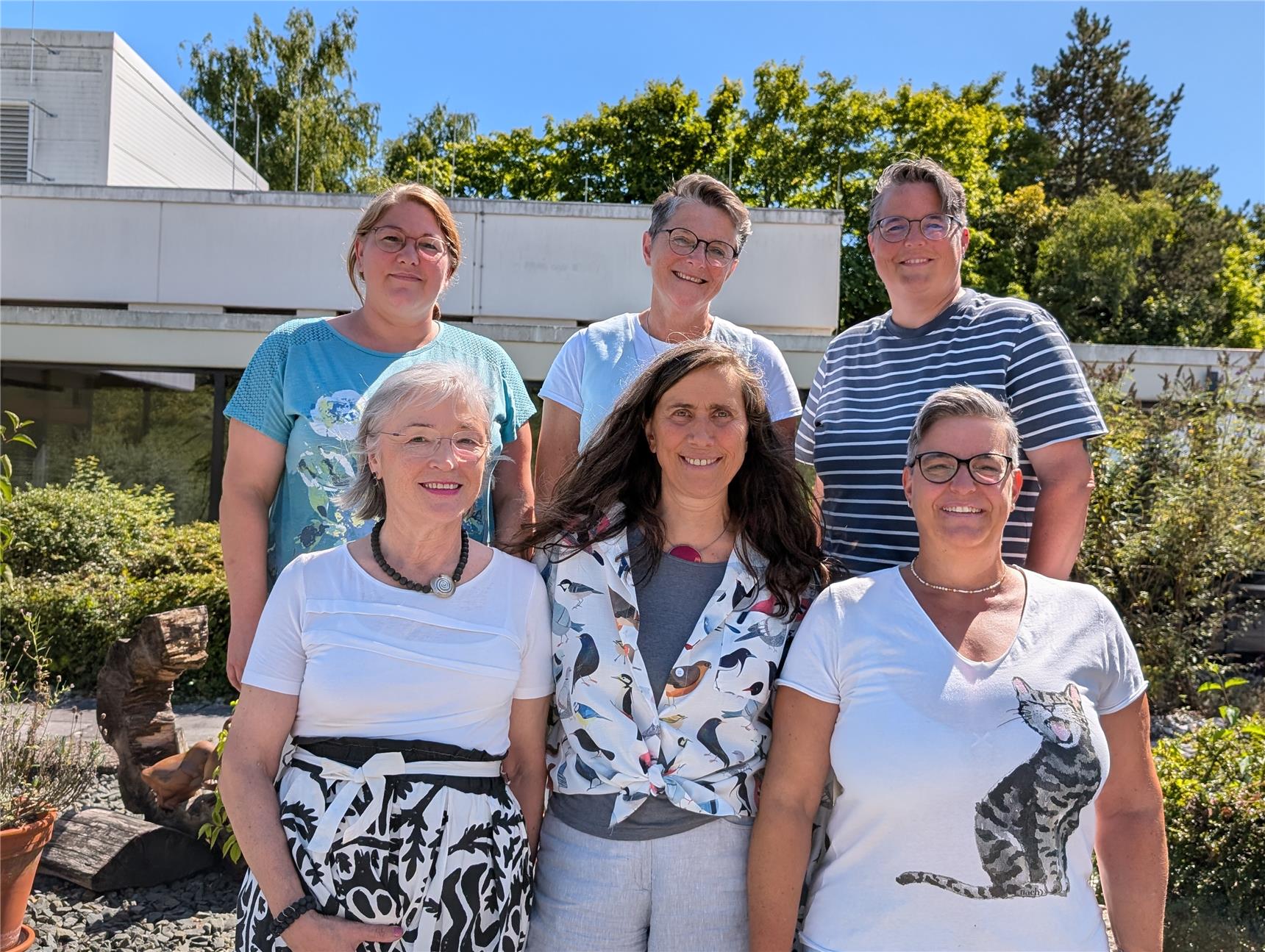 Eine Gruppe von 6 Personen steht in zwei Reihen vor einem Gebäude.
