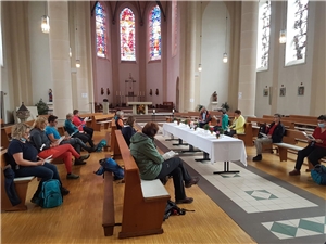 Das Foto zeigt die Mitarbeiternden der Caritas in der Kirche Herz Jesu. In der MItte der Kirche steht ein wundervoll dekorierter Tisch.