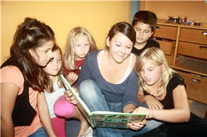 Junge Freiwillige liest Kindern aus einem Buch vor.