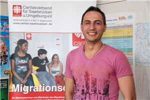 Khalil Raslilo freundlich lachend, vor einem Banner des Migrationsdienstes des Caritasverbands Saarbrücken stehend