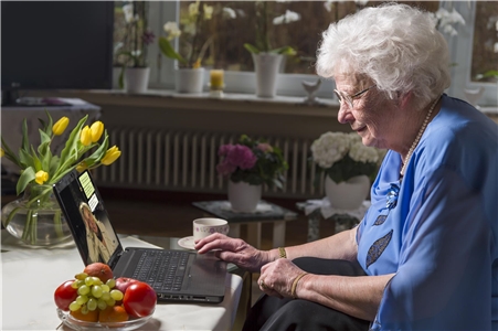 Ältere Frau sitzt in ihrem Wohnzimmer am Laptop