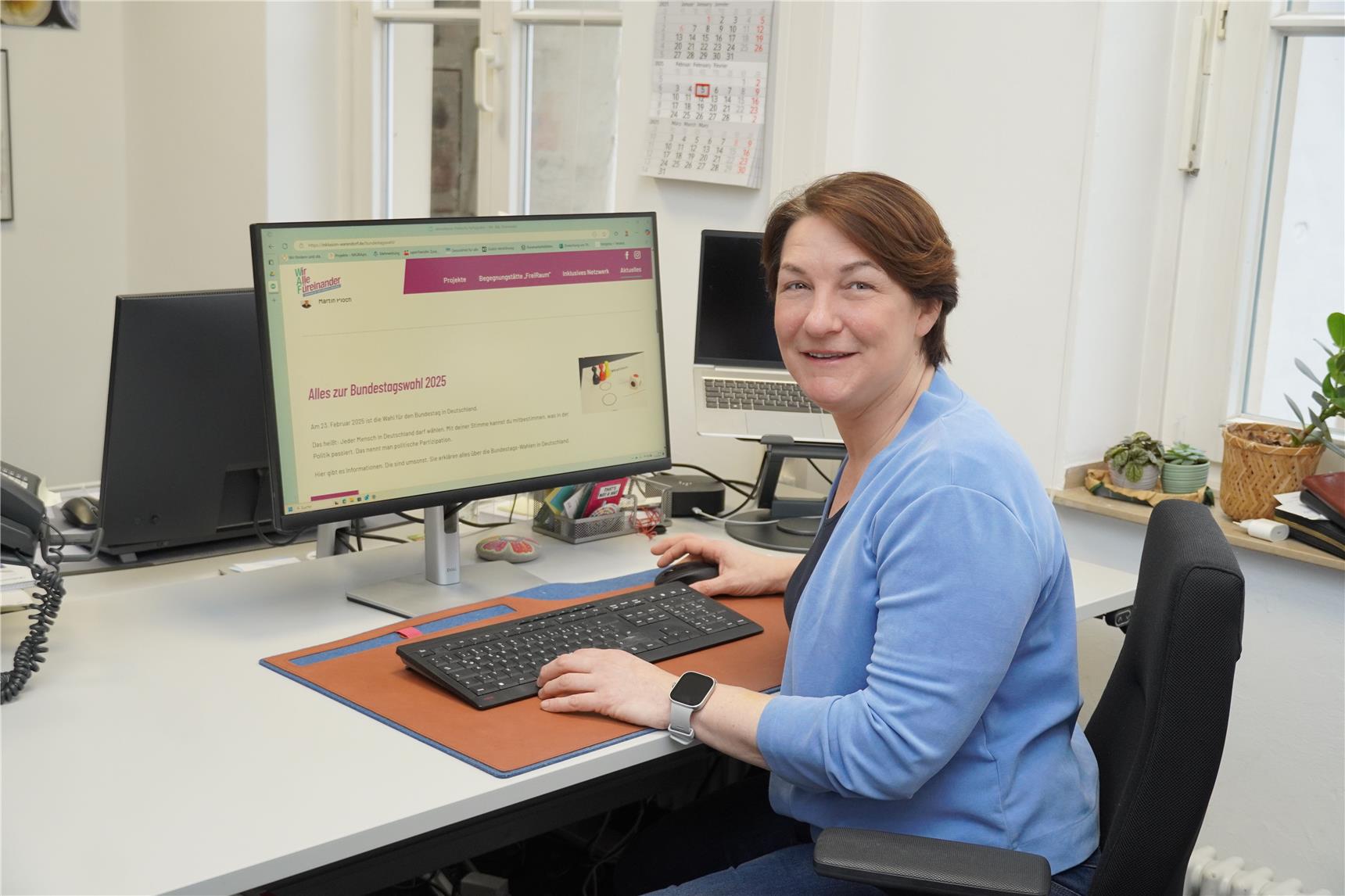 Eine Frau sitzt an einem Schreibtisch und zeigt eine Webseite