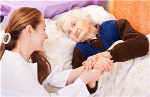 Ältere kranke bettlägerige Frau wird von einer Pflegekraft getröstet