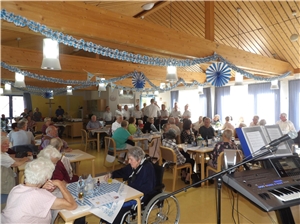 Blick in den blau-weiß geschmückten Saal, wo zahlreiche Tische mit vielen Besuchern zu sehen sind