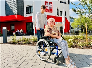 Matteo Thewalt fährt vor dem Altenzentrum eine Bewohnerin im Rollstuhl spazieren.