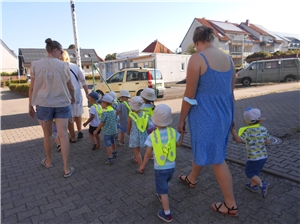 eine Kindergruppe mit gelben Warnwesten wird von Erzieherinnen auf dem Weg zum Spielplatz begleitet