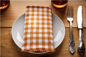 ein weißer Teller mit bunter Serviette auf einem Holztisch, Messer und Gabel rechts daneben