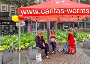 drei Frauen unter einem roten Caritas-Pavillon auf einer Bank