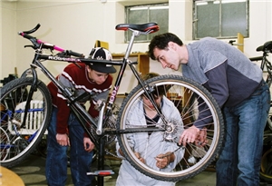 Drei Jundendliche die ein Fahrrad reparieren.