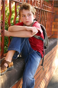 Kleiner Junge mit Rucksack sitz an einem Zaun.
