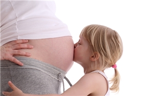 Kind küßt Bauch der schwangeren Mutter.