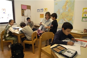 Klassenzimmer mit Stühlen und Tischen, Lehrerin und fünf Schüler.