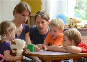 Mann und Frau spielen Würfelspiel mit drei Kindern.
