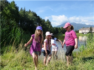 Kinder laufen durchs Gras. Im Hintergrund sind See, Wald und Berge zu sehen. Kindererholung Natz 2015 1
