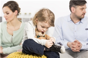 Ein Kind sitzt, mit seinem Teddy im Arm, bedrückt zwischen Mutter und Vater, die jeweils in eine andere Richtung schauen - offensichtlich hatten sie Streit. Kinder aus der Klemme